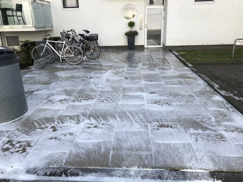 Rensning af fliser foran bygning med cykler